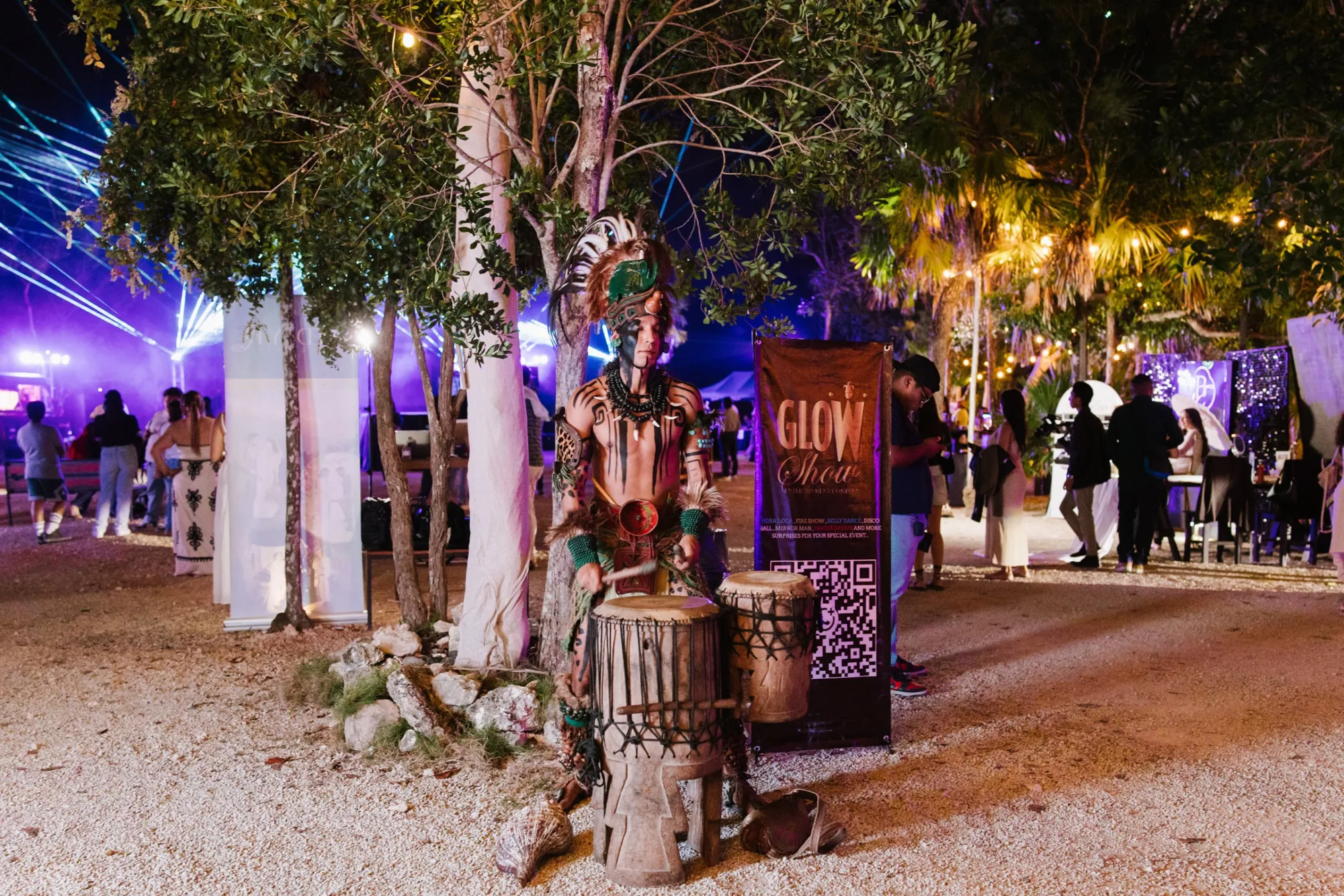 A Mayan drummer in ceremonial dress among the exhibitor pavilion at night