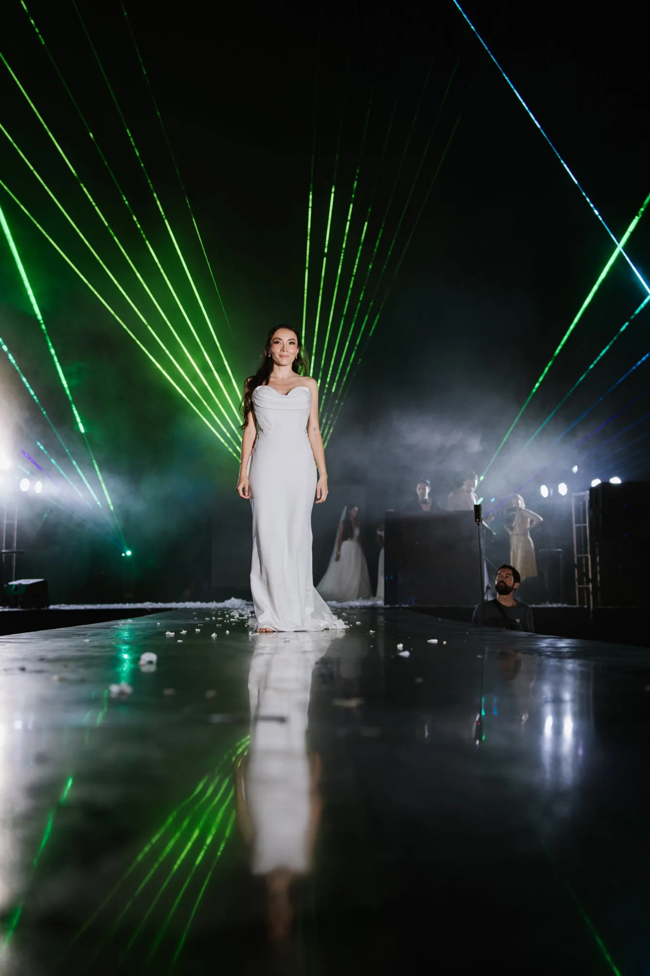 A bride walks the runway in a fitted gown beneath green lasers