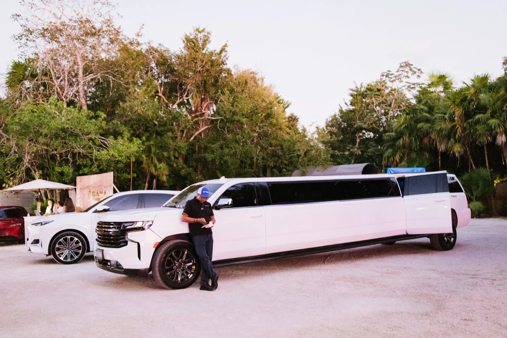 A white stretch limousine and SUV parked at the edge of the jungle