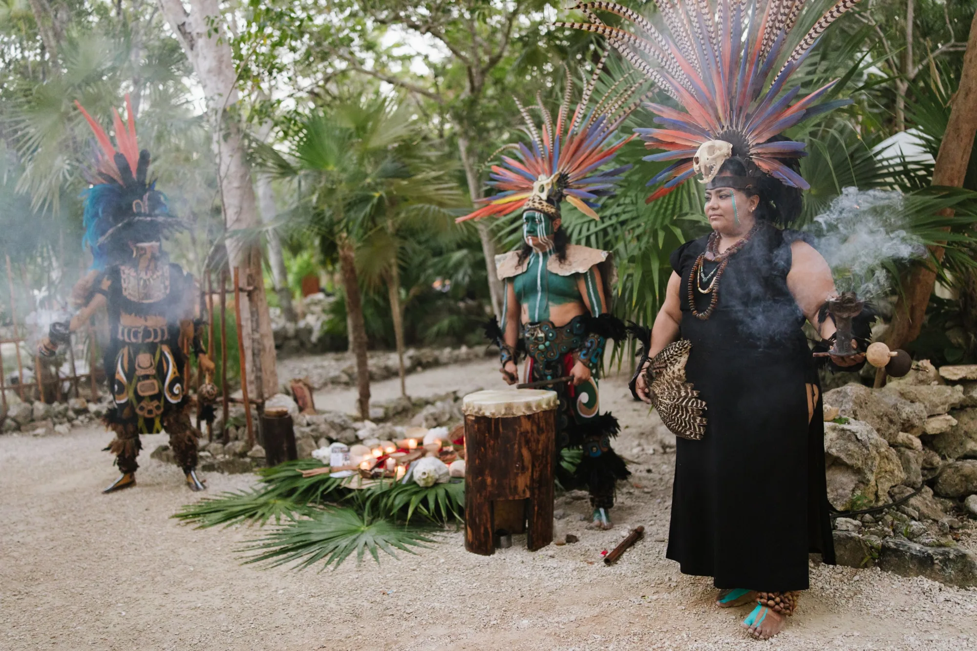 A Mayan ceremony with dancers in feathered headdresses beside an offering of fruit and palm leaves
