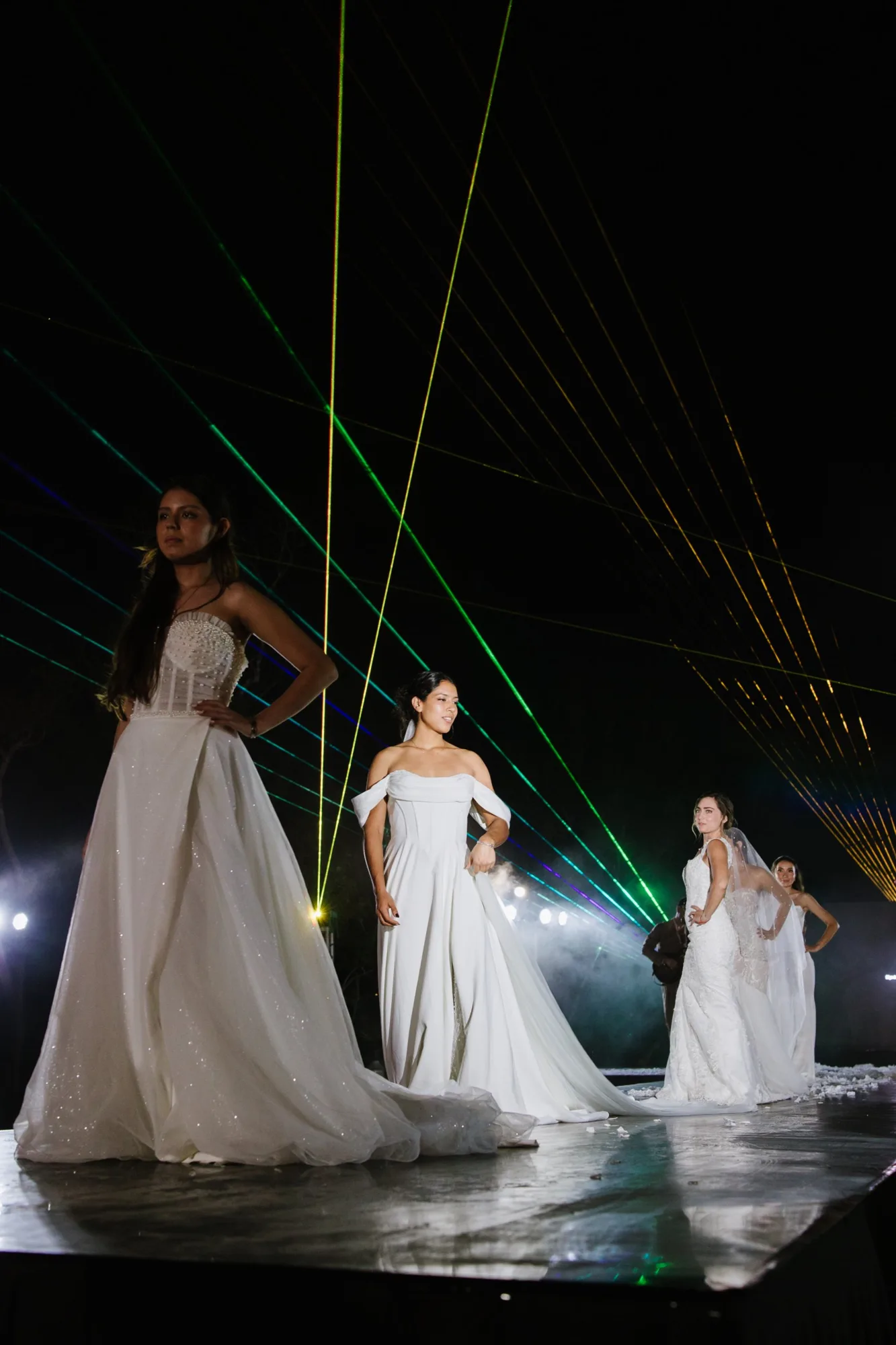 Three brides in white gowns pose together at the end of the runway