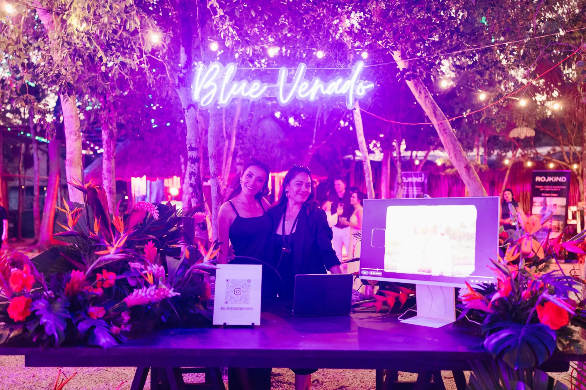 The Blue Venado booth glowing under a neon sign, surrounded by tropical flowers